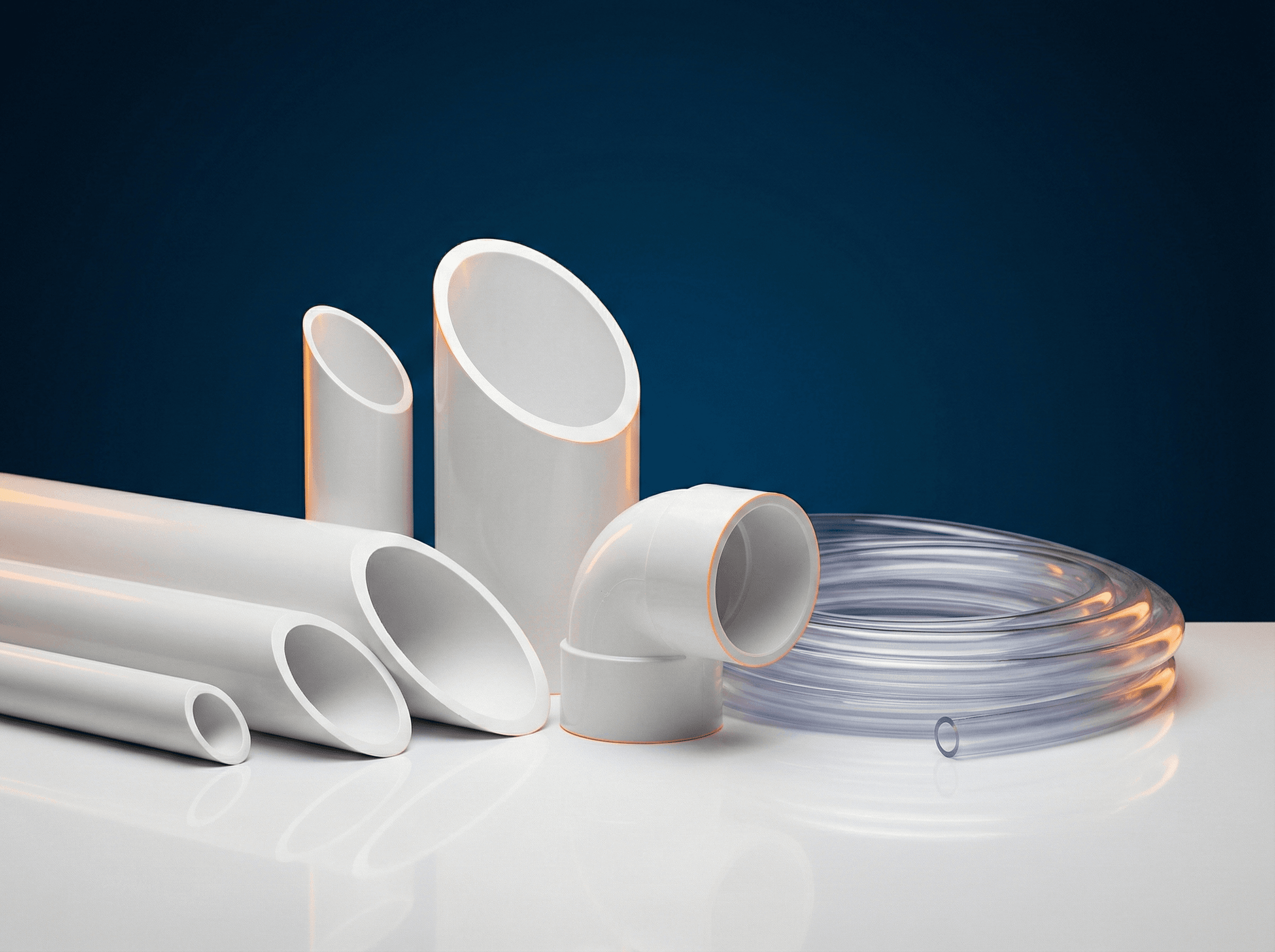 PVC products: white pipes of varying diameters, elbow fitting, and flexible transparent hose